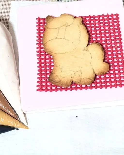 Biscoito em formato de cavalinho, ainda sem cor, ao lado de sacos de confeitar com glacê
