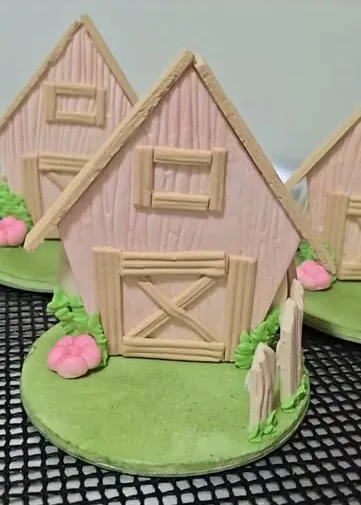 Dois celeiros cor-de-rosa modelados em pasta de leite em pó, com cerquinha e flores, sobre base verde